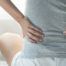 Person med spondylose rygsmerter sidder på gulvet og strækker ud i ryggen.