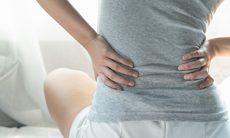 Person med spondylose rygsmerter sidder på gulvet og strækker ud i ryggen.